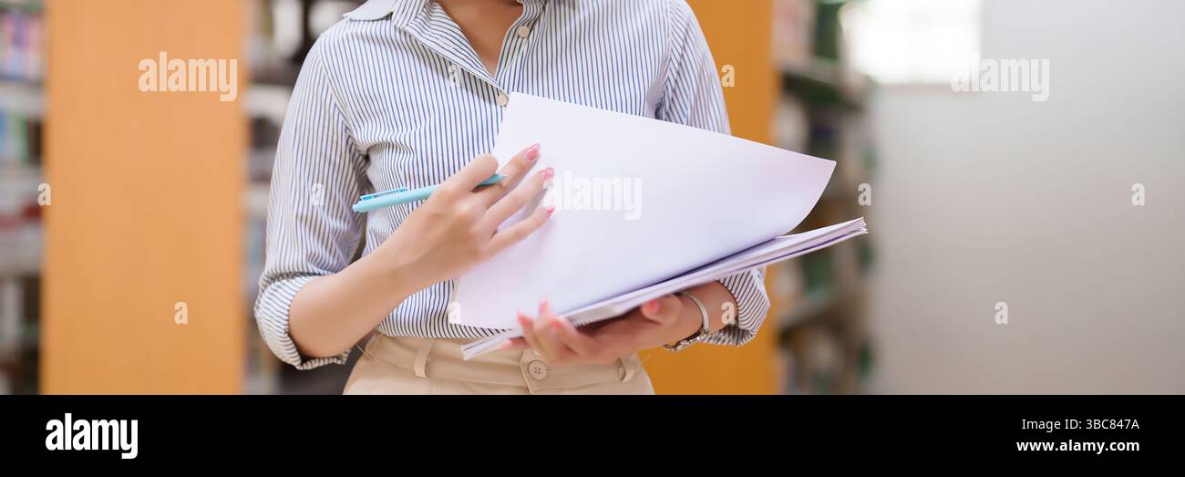 Bild einer erwachsenen asiatischen Lehrerin, die Dokumente in einer Schulbibliothek hält und überprüft. Dieses Bild zeigt Bildung, Lernen, Lehren und t Stockfoto