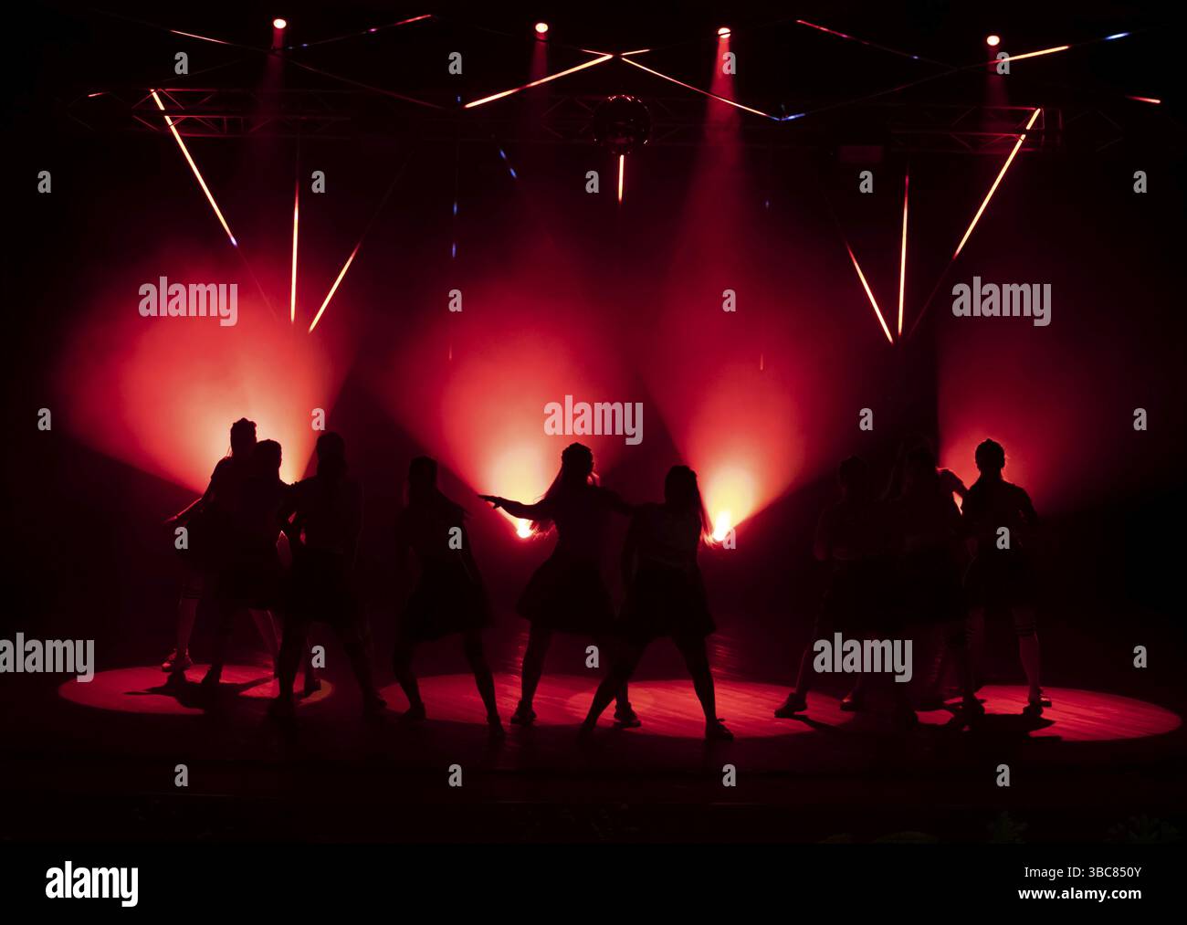 Dunkle Silhouetten von tanzenden Mädchen vor dem Hintergrund des roten Lichtes der Bühnenbeleuchtung Stockfoto