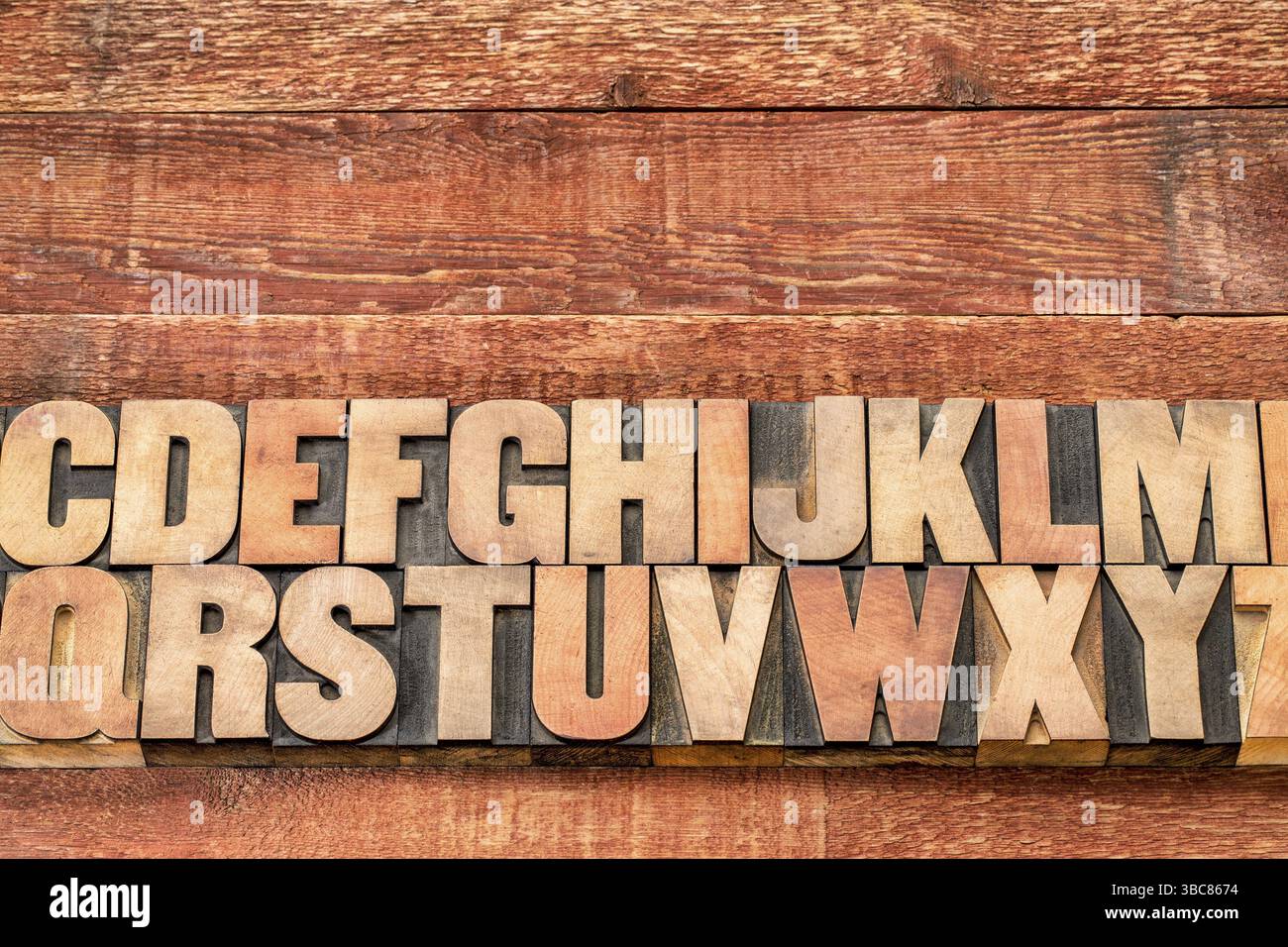 Abstraktes Alphabet in Vintage-Buchdruckblöcken gegen rustikal rot lackiertes Scheunenholz mit Kopierraum Stockfoto