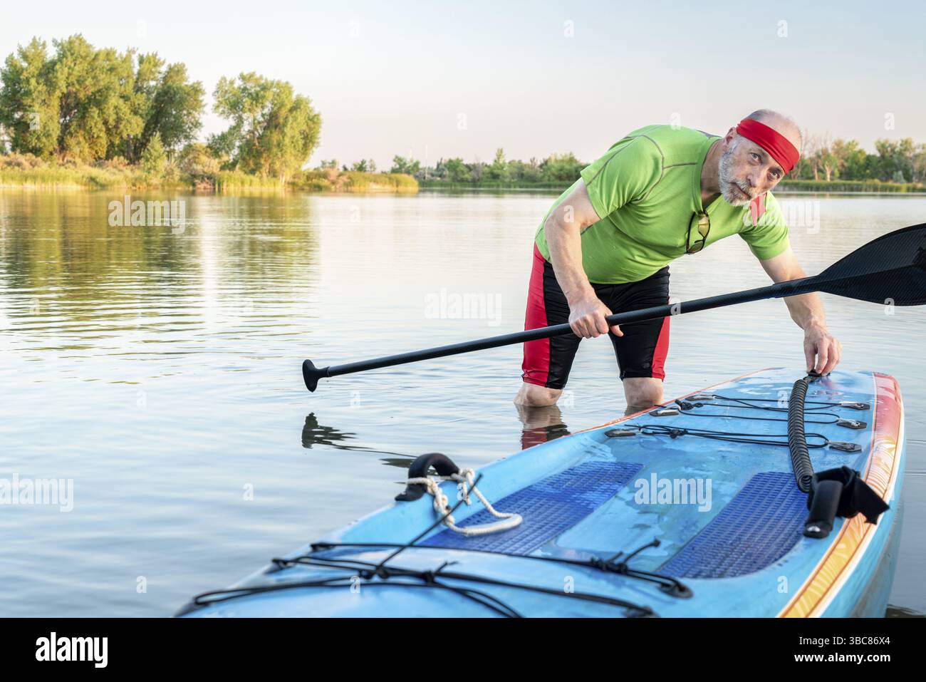 Umwelt Portrait eines älteren männlichen Paddler mit einem Stand up paddleboard an einem ruhigen See im Norden von Colorado, Sommer Landschaft Stockfoto