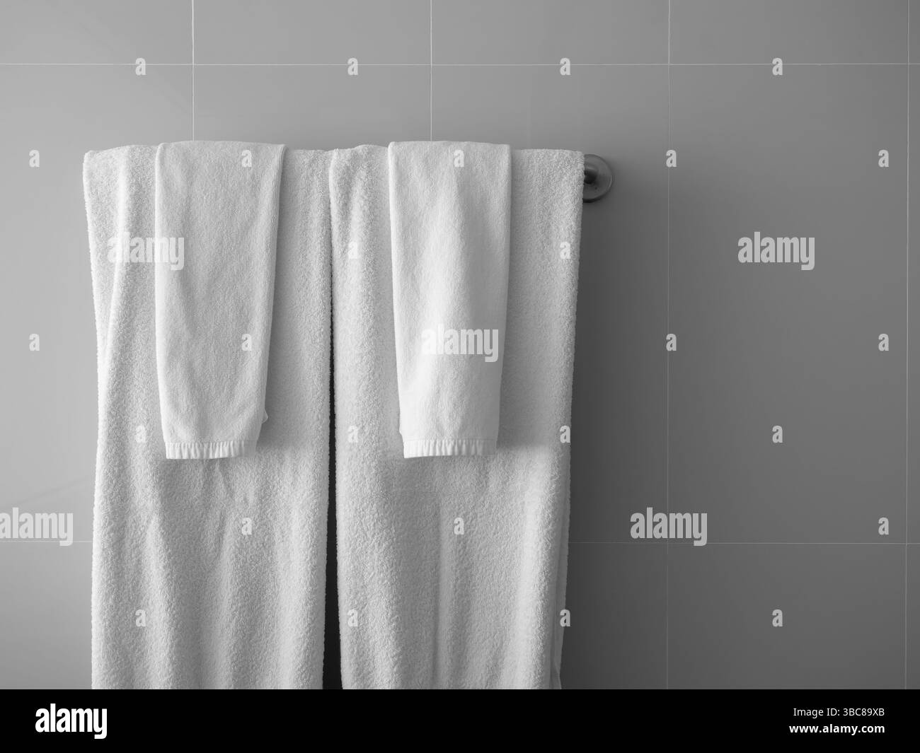 Paare Set aus großen und kleinen sauberen weißen Handtüchern, gefaltet an einem Metallbügel, graue Fliesen an der Ecke des Badezimmers, waagerecht hintergraut Stockfoto