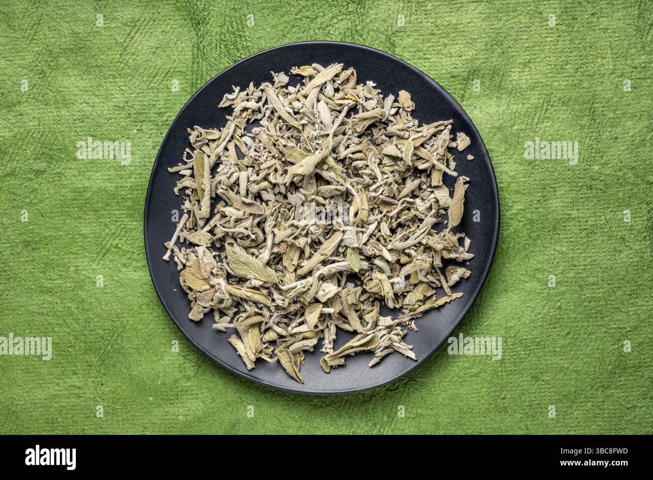 Trockener griechischer Salbeikräutertee (Fascomilo) auf einer schwarzen Platte auf grünem, strukturiertem Rindenpapier Stockfoto