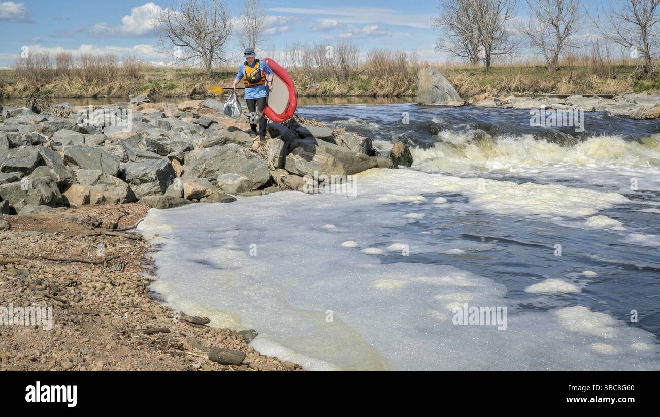 Senior Paddler transportiert aufblasbares Stand Up Paddleboard über einen schnellen South Platte River in der Frühjahrslandschaft mit niedrigem Wasserfluss Stockfoto