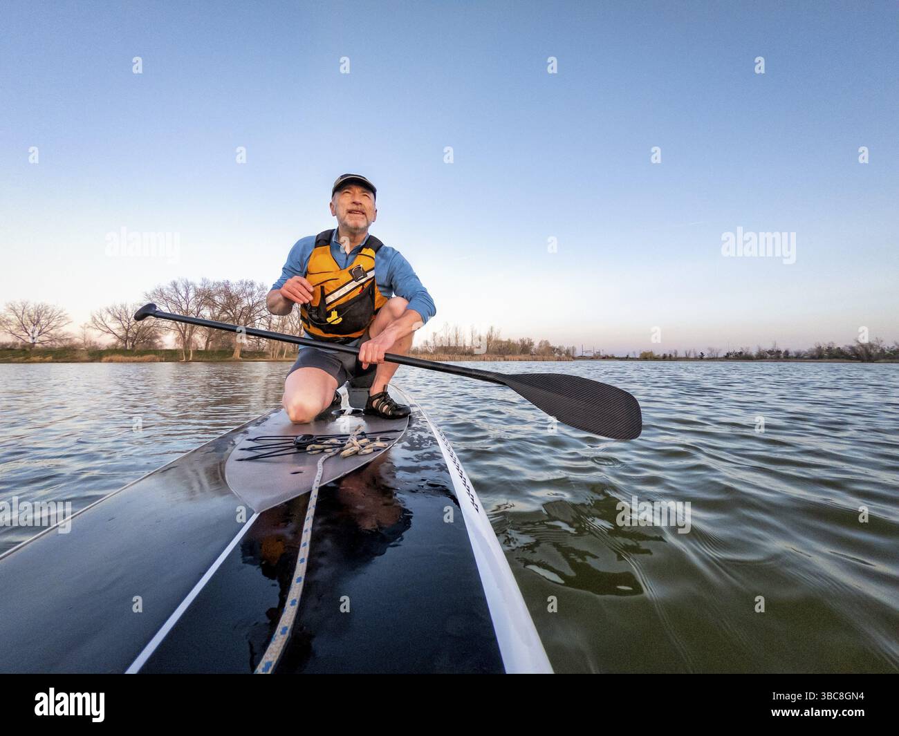 Sportlicher Seniorenmann auf einem Stand-Up-Paddleboard, der Sonnenuntergangsliebhaber an einem ruhigen See in Colorado mit Bugblick genießt Stockfoto