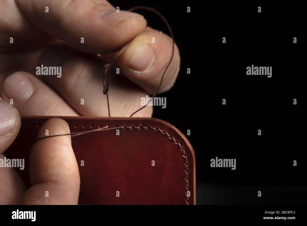 Herstellung von Ledergeldbörsen. Die Hände des Meisters nähen ein Lederprodukt Stockfoto