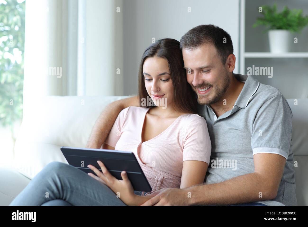 Paare, die sich Medien auf einem Tablet ansehen, sitzen auf einem Sofa zu Hause Stockfoto
