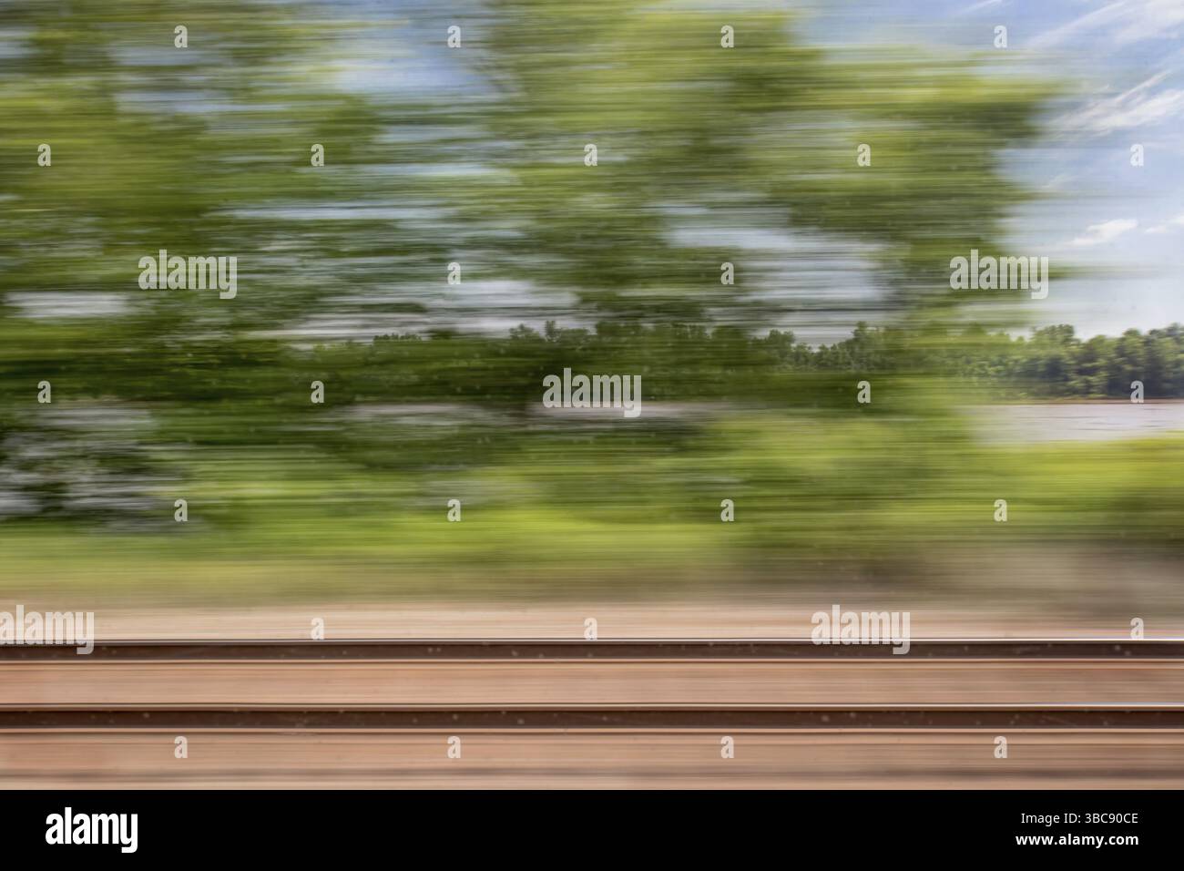 Verschwommene abstrakte Landschaft aus Eisenbahngleisen und einem Fluss, der vom Zugfenster aus in Bewegung ist Stockfoto