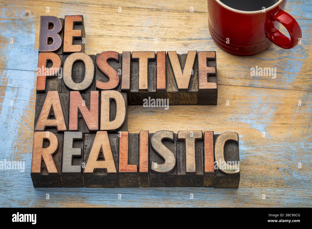 Seien Sie positiv und realistisch – motivierender Text in Vintage-Buchdruckblöcken aus Holz Stockfoto