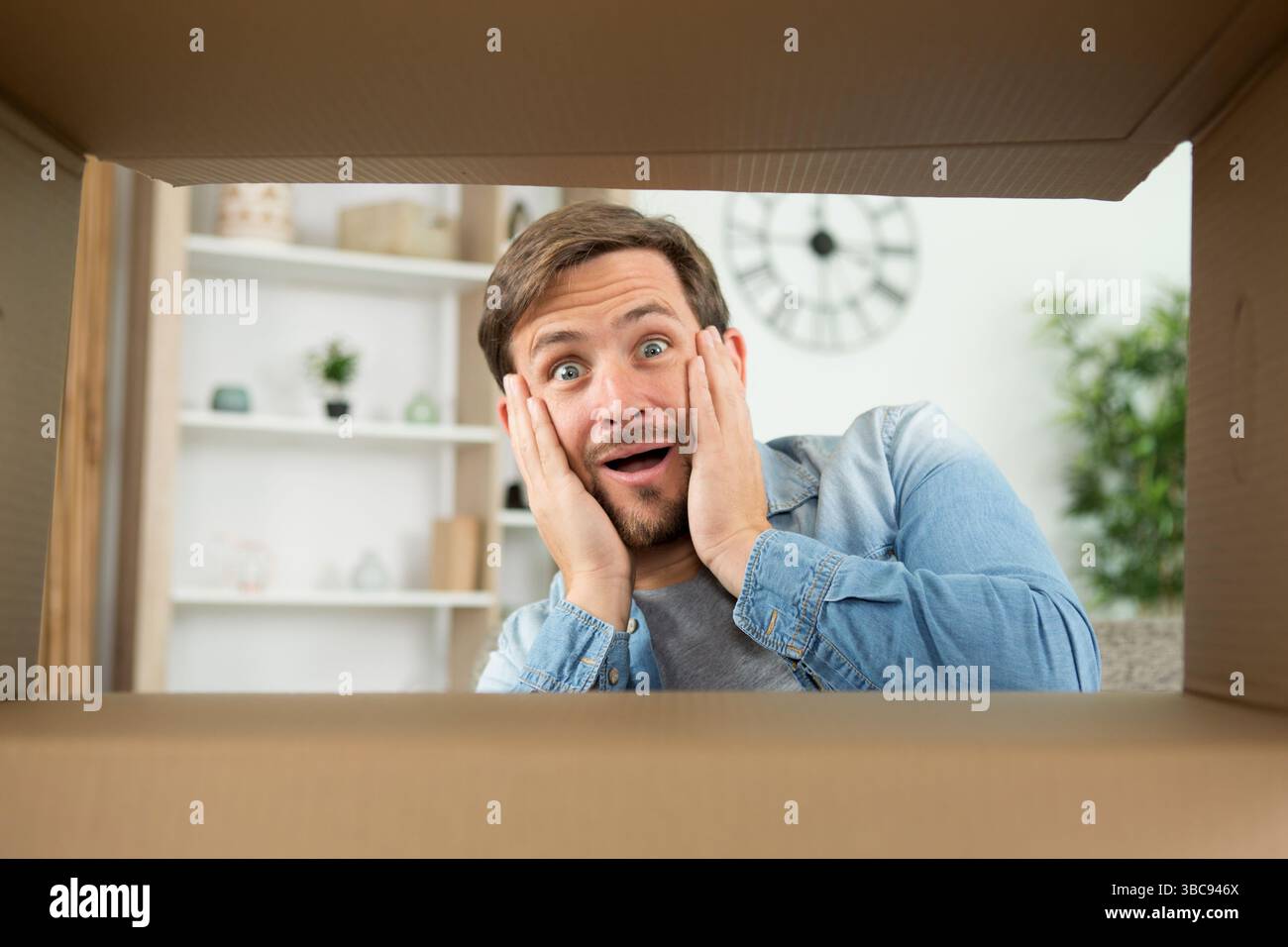 Ein überraschter Mann packt den aufklappbaren Karton aus Stockfoto
