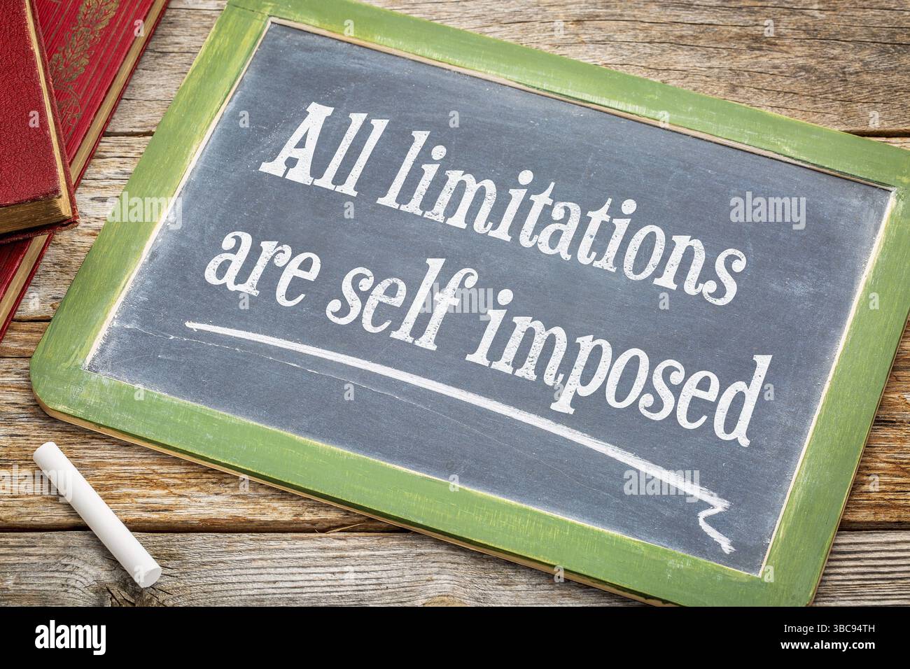 Alle Einschränkungen sind selbst auferlegt - inspirierende Aussage auf einer Tafel mit weißer Kreide und einem Stapel Bücher auf einem rustikalen Holztisch Stockfoto