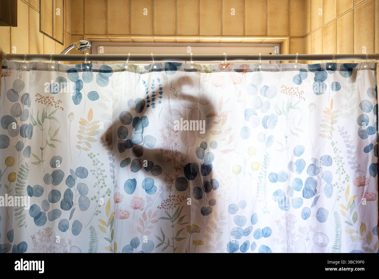 Die Silhouette eines Mannes, der duscht, durch einen Duschvorhang im Badezimmer des Appartements gesehen. Natürliche Hintergrundbeleuchtung, Schattenaufdruck auf der Cur Stockfoto