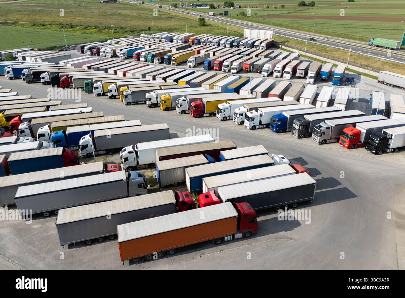 Aus der Vogelperspektive eines großen LKW-Parkplatzes an einem Logistikzentrum mit mehreren gewerblichen Sattelzügen, die in organisierten Reihen geparkt sind. Stockfoto