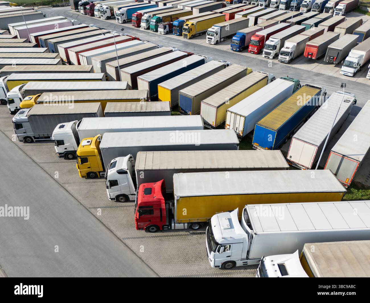 Aus der Vogelperspektive eines großen LKW-Parkplatzes an einem Logistikzentrum mit mehreren gewerblichen Sattelzügen, die in organisierten Reihen geparkt sind. Stockfoto