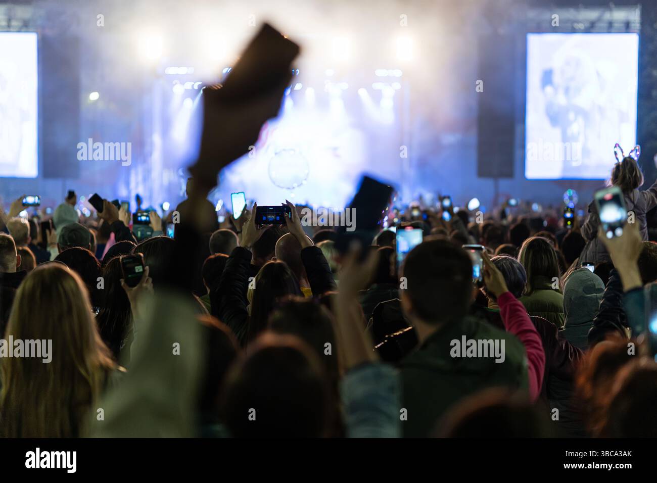 Streamen eines Musikkonzerts über ein Smartphone in soziale Medien. Das Publikum winkt beim Nachtkonzert. Silhouetten von Menschen von hinten. Stockfoto