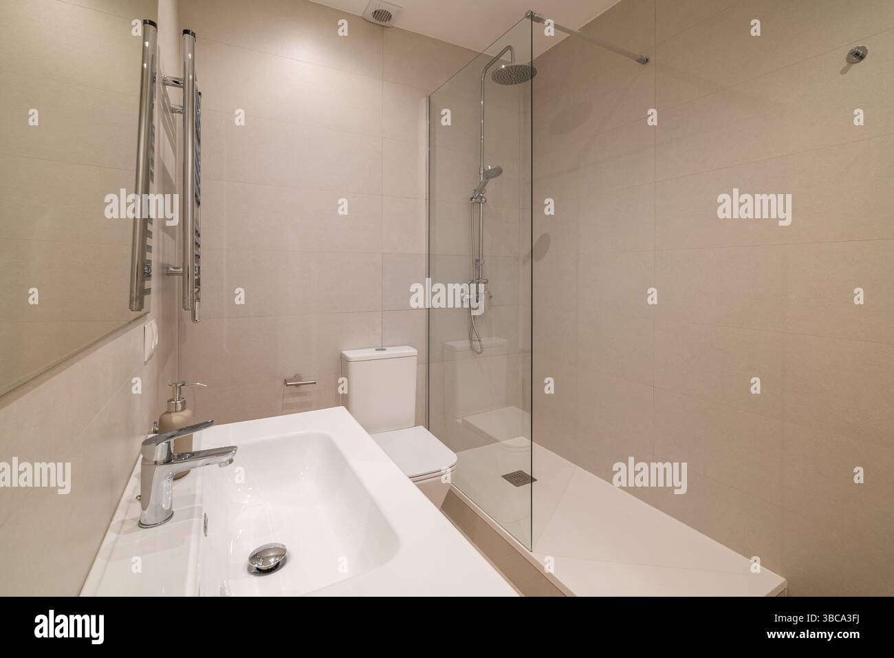 Beigefliestes Badezimmer mit Glasduschtrennwand und Chrom-Regenduschkopf Stockfoto