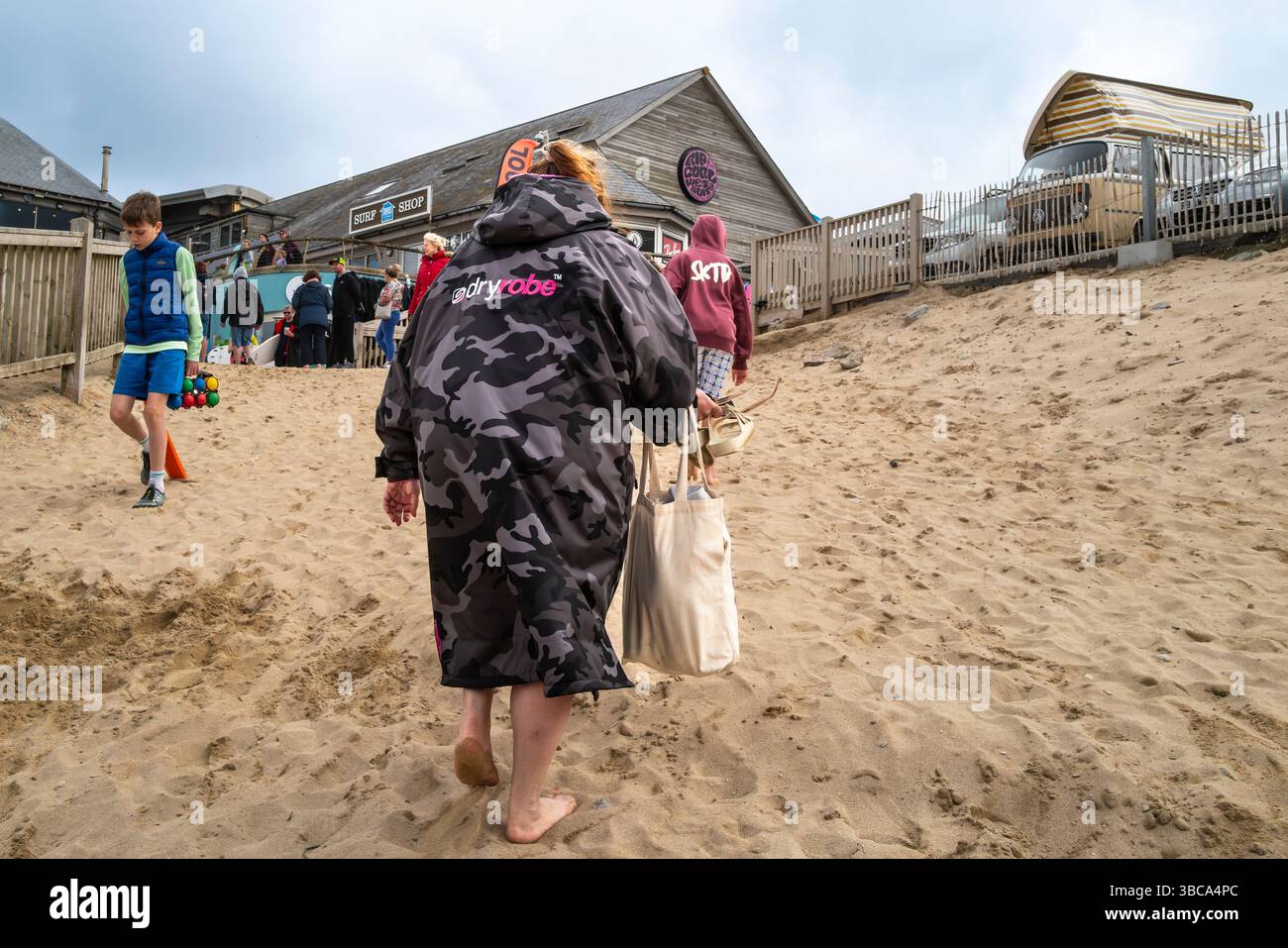 Eine Urlauberin mit Dryrobe verlässt und geht nach einem Tag am Fistral Beach in Newquay in Cornwall in Großbritannien nach Hause. Stockfoto