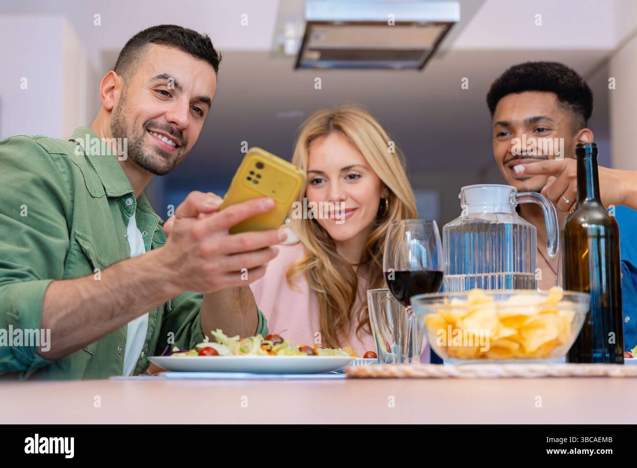 Fröhliche multiethnische Freunde genießen Snacks und Getränke in moderner, heller Küche Stockfoto