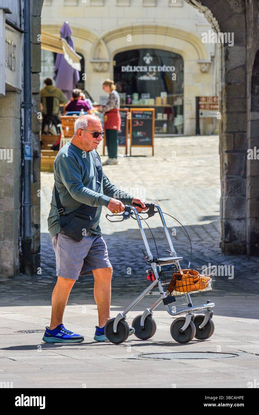Älterer Mann in Shorts, der mit Hilfe eines fahrbaren Gehgestells läuft - Loches, Indre-et-Loire (37), Frankreich. Stockfoto