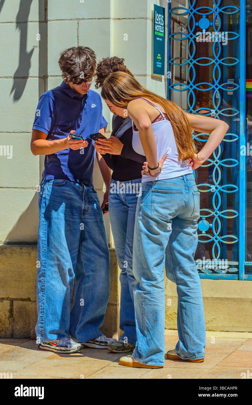 Drei junge Menschen, die sich auf ihrem Smartphone Informationen ansehen oder vergleichen - Loches, Indre-et-Loire (37), Frankreich. Stockfoto