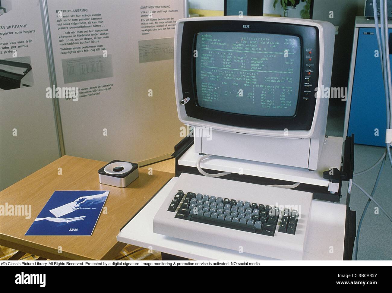 IBM Computer, 1978. Eine Workstation mit Monitor auf einem Schreibtisch mit Tastatur, eine Bedienungsanleitung und ein Aschenbecher an der Seite. Ein Bildschirm im Hintergrund beschreibt die Software, die für die Ladenplanung und Bestandsverwaltung in Lebensmittelgeschäften verwendet wird, und wie das Computersystem die Rentabilität steigern soll. Der typische IBM-Computer der späten 1970er Jahre war ein robuster, spezialisierter Computer, der für das geschäftliche und institutionelle Computing von zentraler Bedeutung war. Das Design, die Software und die Anwendungen – wie die für die Verwaltung von Lebensmittelgeschäften – unterstrichen die Rolle von IBM bei der Gestaltung moderner Datenverarbeitung Stockfoto
