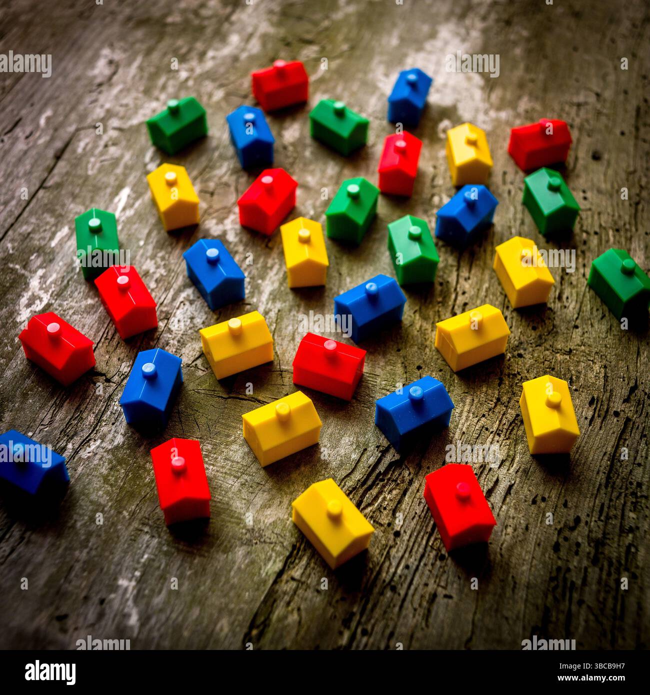 Zahlreiche kleine, lebhafte Häuser sind auf einer strukturierten Holzoberfläche verstreut und erinnern an die lebendige Energie eines klassischen Immobilienbrettspiels Stockfoto