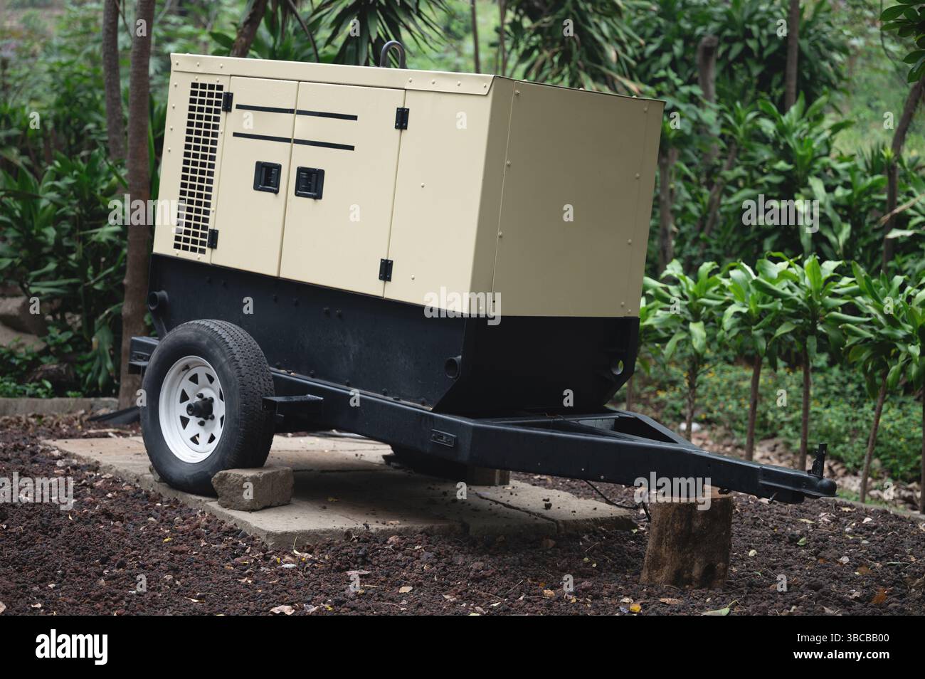 Der tragbare Generator befindet sich auf einem Betonsockel, umgeben von lebendigen Pflanzen im sonnigen Außenbereich. Stockfoto