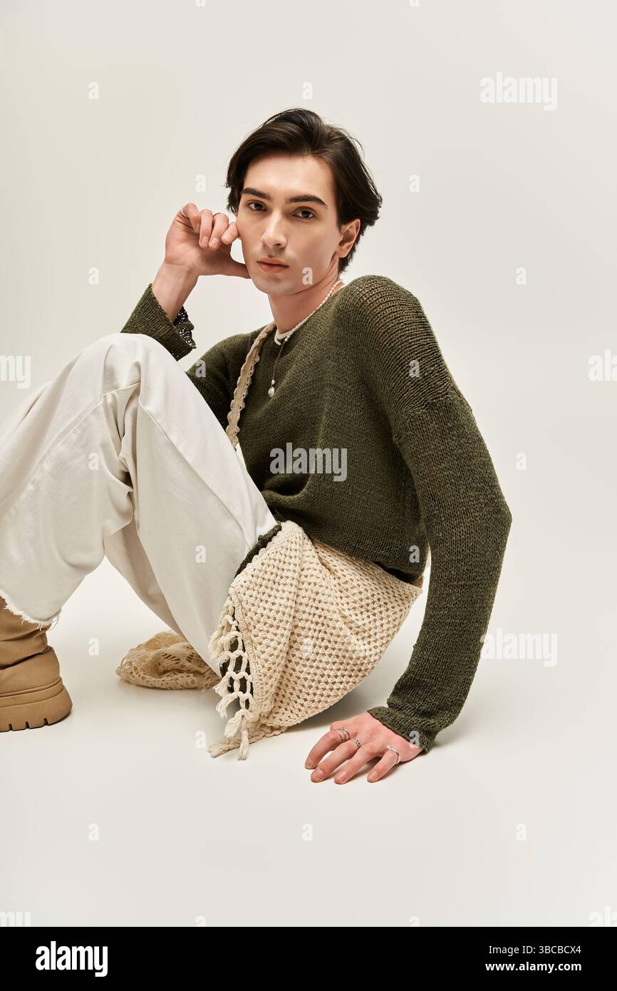 Eine junge nicht-binäre Person posiert elegant auf dem Boden und zeigt ihr schickes Outfit. Stockfoto