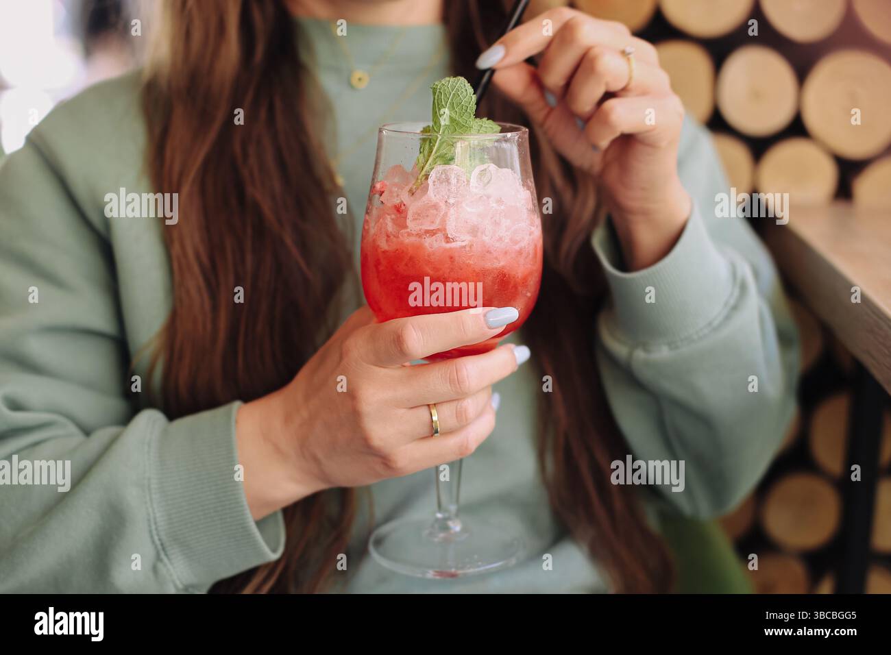 Erfrischender roter Cocktail mit Eis. Frau, die den Drink in der Hand hält. Sommergetränk mit Minzblättern. Elegantes Glas mit Strohhalm. Chillen im Café. Stockfoto