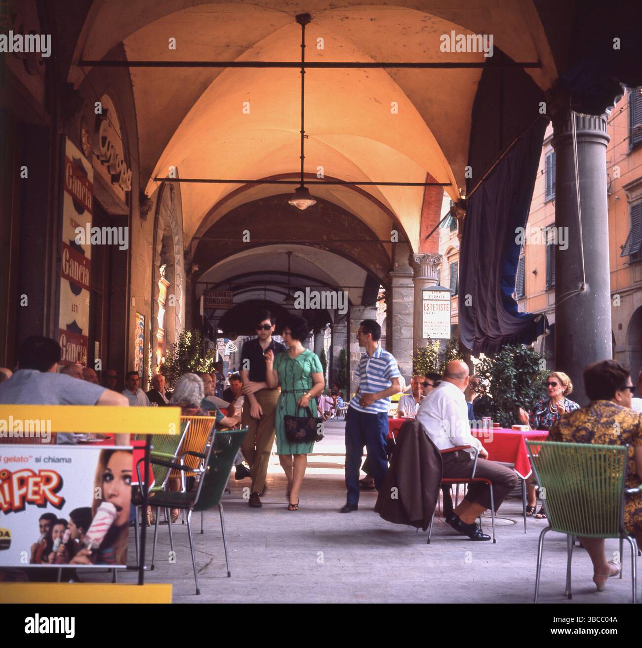 1964 Menschen in einem Café oder einer Gelateria unter den Arkaden in der Via Gugliemo Oberdan, Pisa, Toskana, Italien. Stockfoto