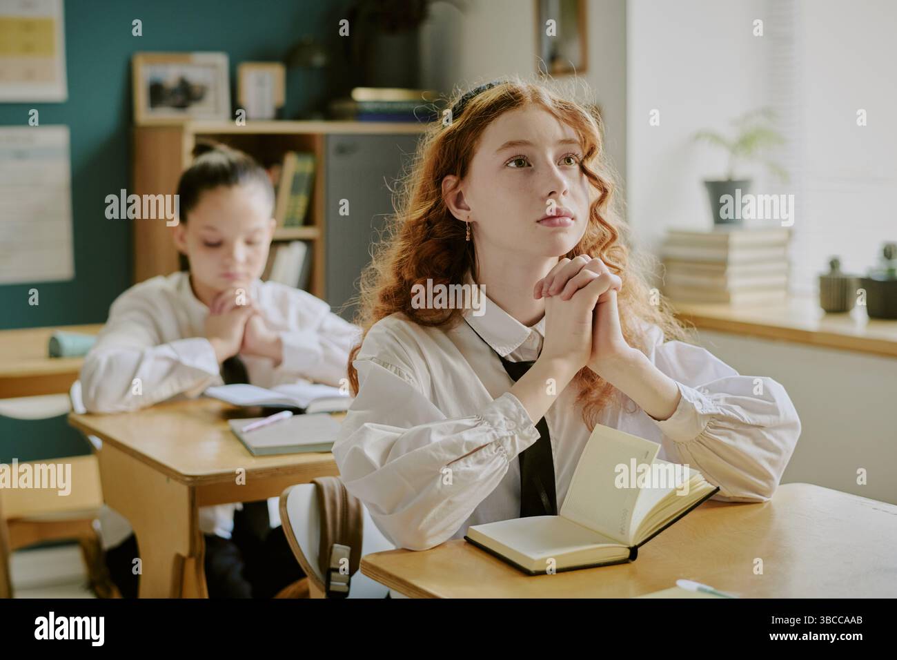 Schüler, die sich mit Büchern, Notizbüchern und Schreibtischen im Unterricht beschäftigen, lernen. Helle Beleuchtung unterstreicht die gediegene Atmosphäre Stockfoto