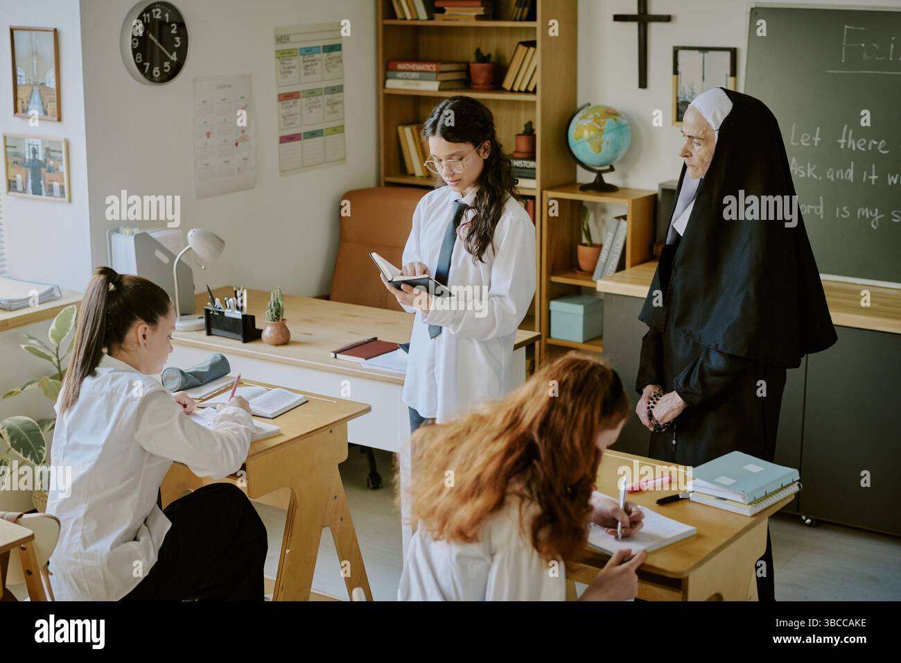 Studenten und Nonnen, die sich mit Büchern und Schreibwaren auf Schreibtischen an pädagogischen Aktivitäten im Klassenzimmer beteiligen. Klassenzimmer mit Wanddekoration Stockfoto