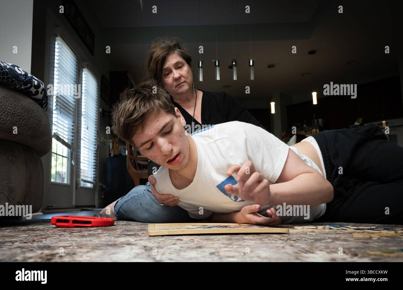 Ft. Mill, South Carolina, USA. März 2025. Beth Hodges begleitet ihren 19-jährigen Sohn Jack auf dem Wohnzimmerboden, während er mit einem einfachen Puzzle spielt. Er hat einen seltenen Krampfanfall namens Dravet-Syndrom sowie Autismus der Stufe 3. (Kreditbild: © Robin Rayne/ZUMA Press Wire) NUR REDAKTIONELLE VERWENDUNG! Nicht für kommerzielle ZWECKE! Stockfoto