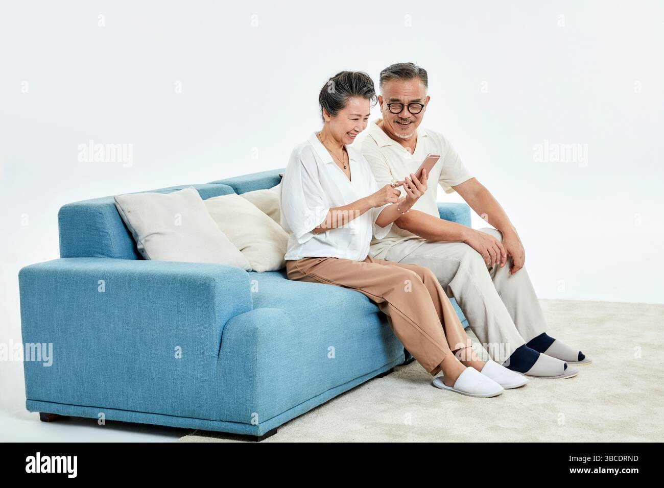 Ein älteres Ehepaar, das auf der Couch sitzt und ihre Telefone benutzt Stockfoto