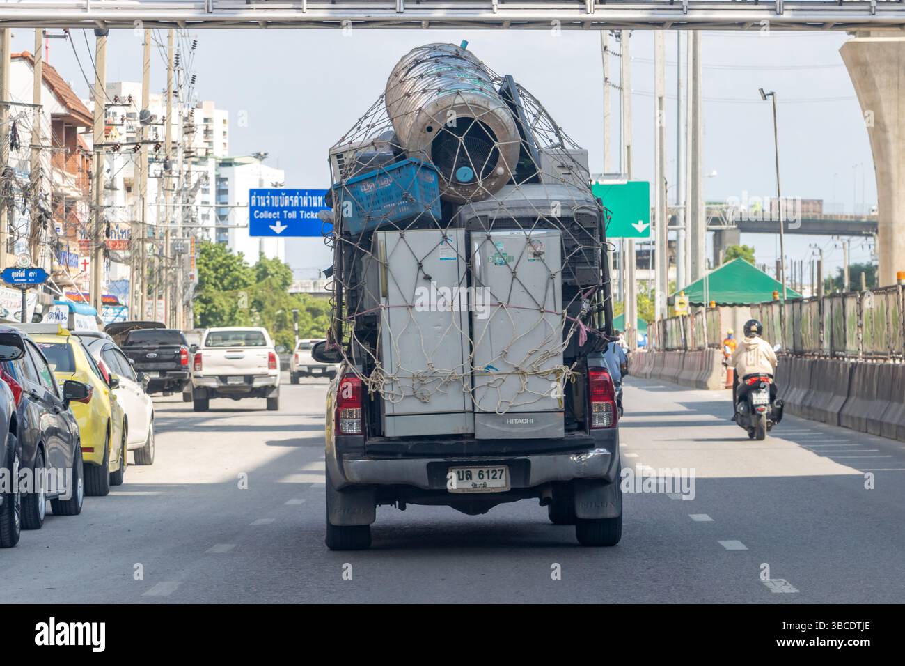 SAMUT PRAKAN, THAILAND, 28. April 2025, Ein schwer beladener Pickup-Truck, der Geräte und andere Gegenstände auf einer stark befahrenen Stadtstraße transportiert Stockfoto