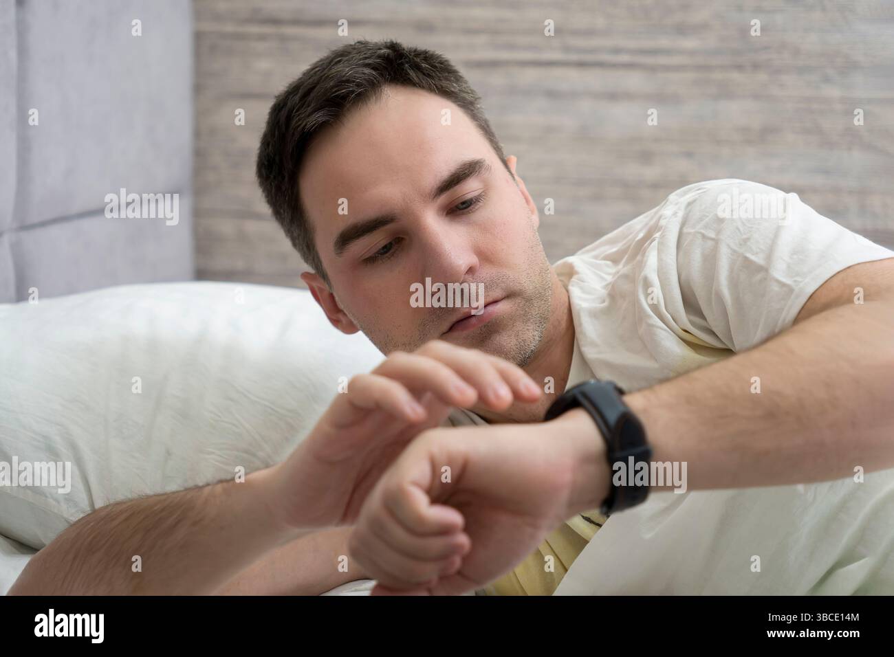 Ein Mann wacht morgens auf und schaut auf seine Uhr. Früher Aufstieg. Moderne, schwarze Smart-Uhr am Handgelenk. Herzschlagüberwachung mit einem intelligenten Gadget in einem dr Stockfoto