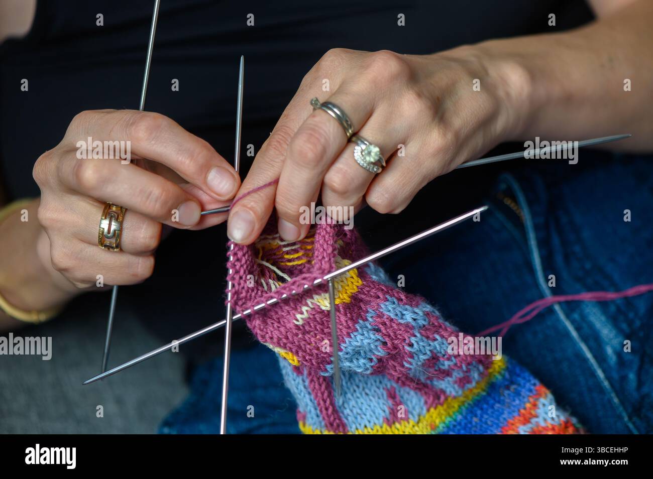 Nahaufnahme einer Frau, die bunt gemusterte Socken von Hand strickt. Handgefertigtes Kunsthandwerk bei Tageslicht. Stockfoto