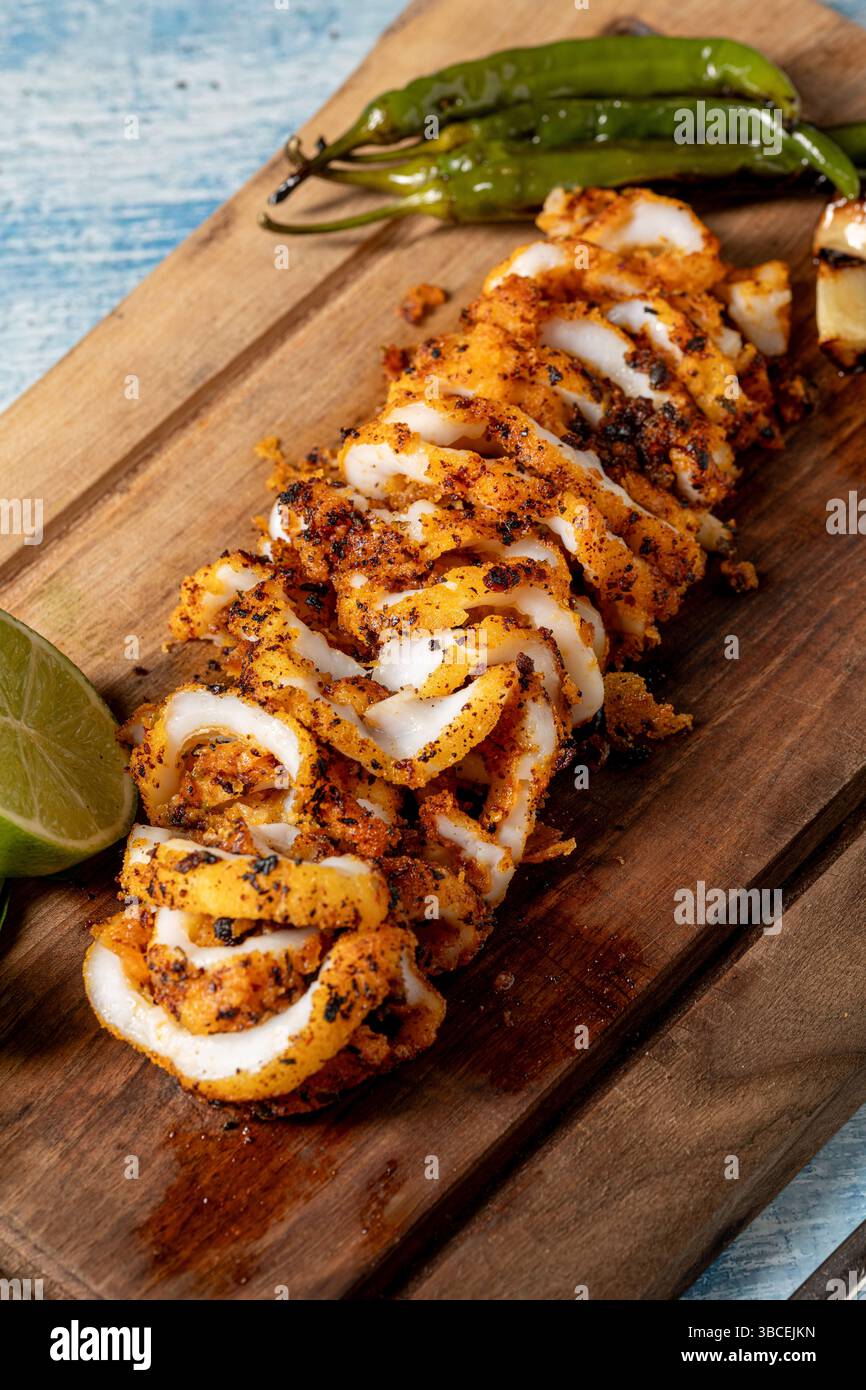 Gegrillte Calamari in Ringe geschnitten mit Garnituren auf einem Holzschneidebrett Stockfoto