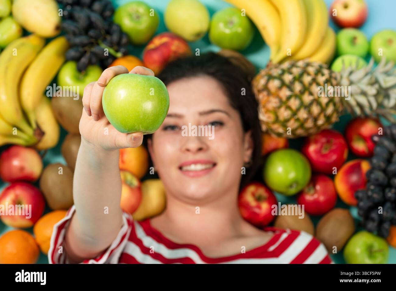 Porträt einer jungen brünetten Frau, die in der Nähe von Früchten liegt und grünen Apfel in der Hand hält. Hochwertige Fotos Stockfoto