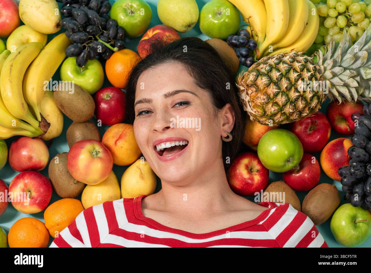 Porträt einer jungen brünetten Frau, die in der Nähe von Früchten liegt und grünen Apfel in der Hand hält. Hochwertige Fotos Stockfoto