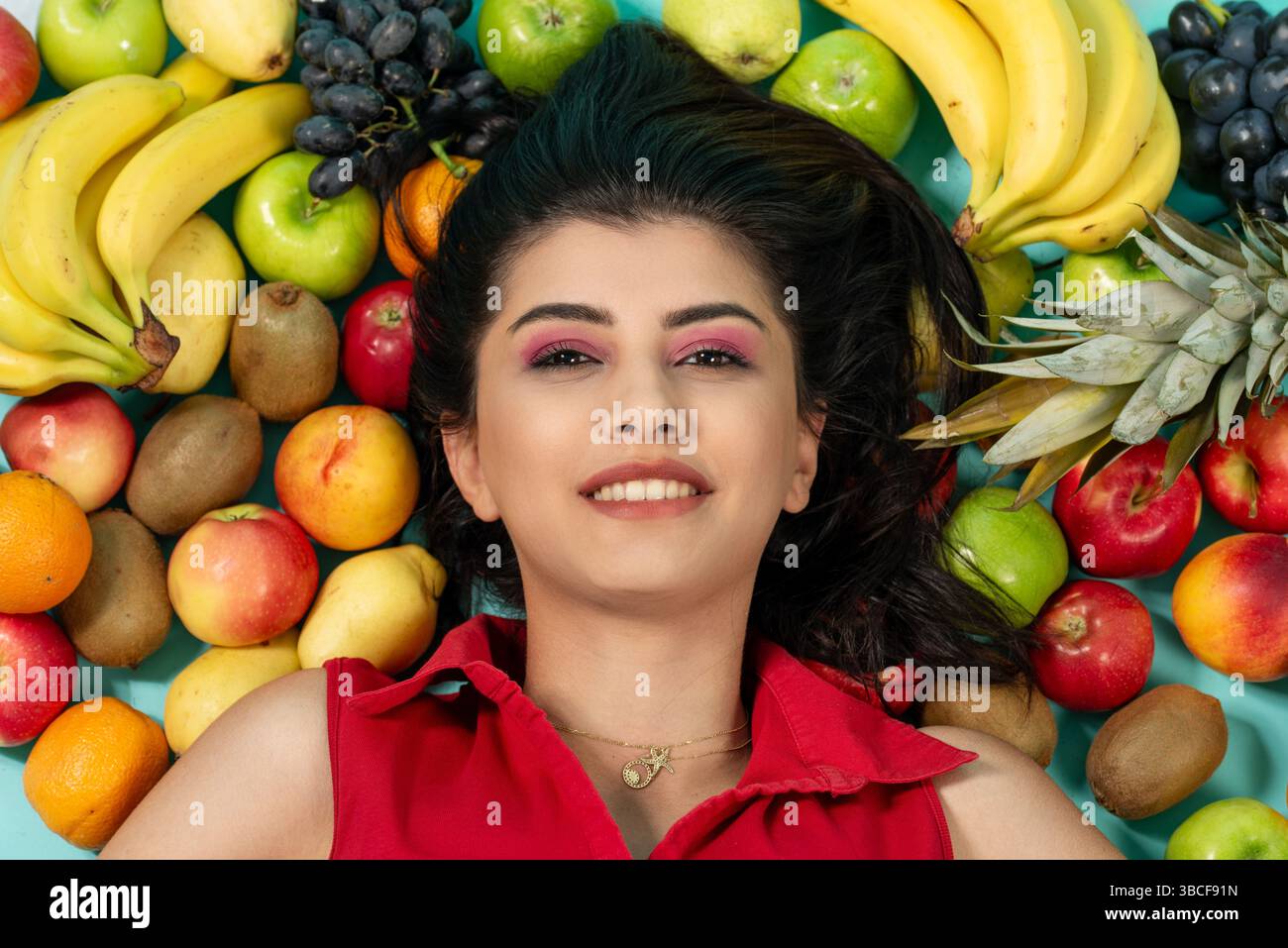 Porträt einer jungen brünetten Frau, die in der Nähe von Früchten liegt und grünen Apfel in der Hand hält. Hochwertige Fotos Stockfoto