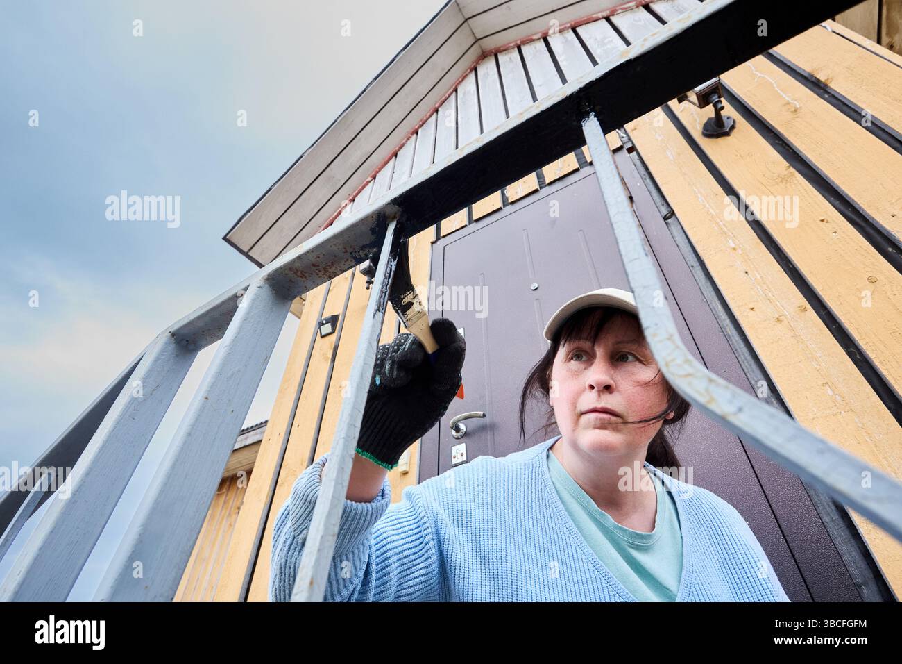 Mit einem kleinen Pinsel Schutzbeschichtung auf Metallstangen in der Veranda Geländer Frau Hauseigentümerin lackiert dekorative Elemente unabhängig. Stockfoto