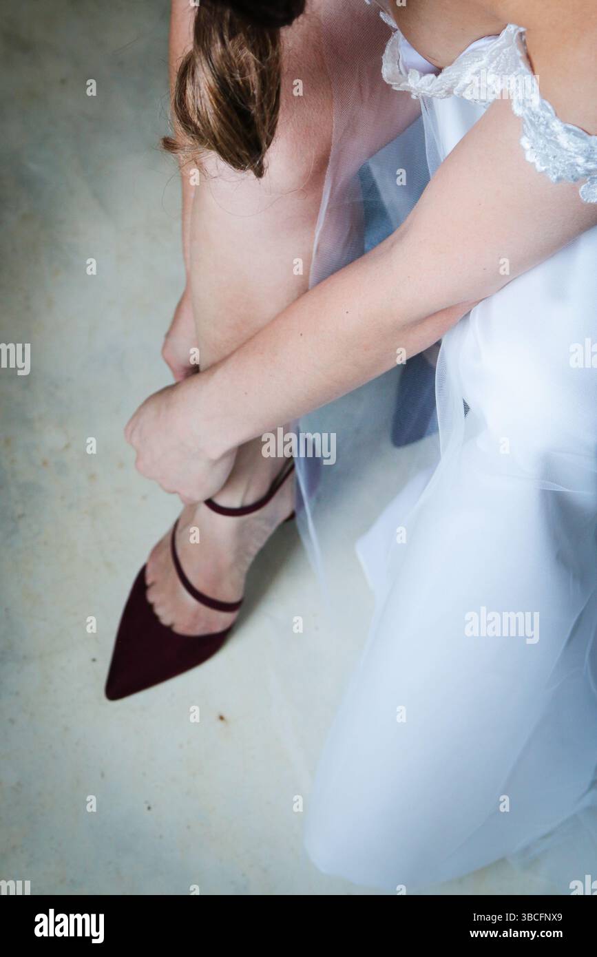 Braut, die ihre burgunderroten Schuhe von oben anschnallt Stockfoto