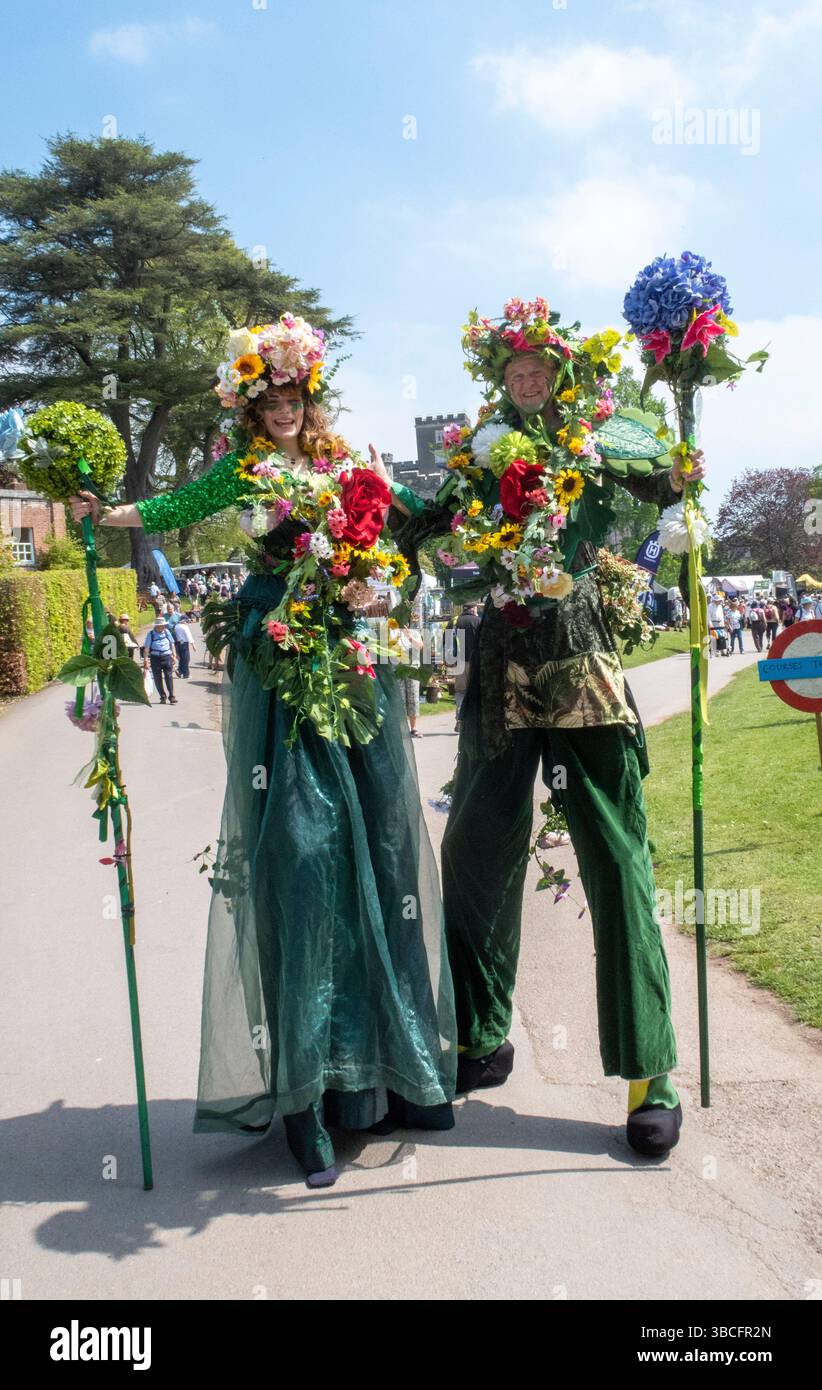 Menschen auf Stelzen in Blumenkostümen beim Toby's Garden Show Festival in Powderham Castle, Devon, Großbritannien Stockfoto