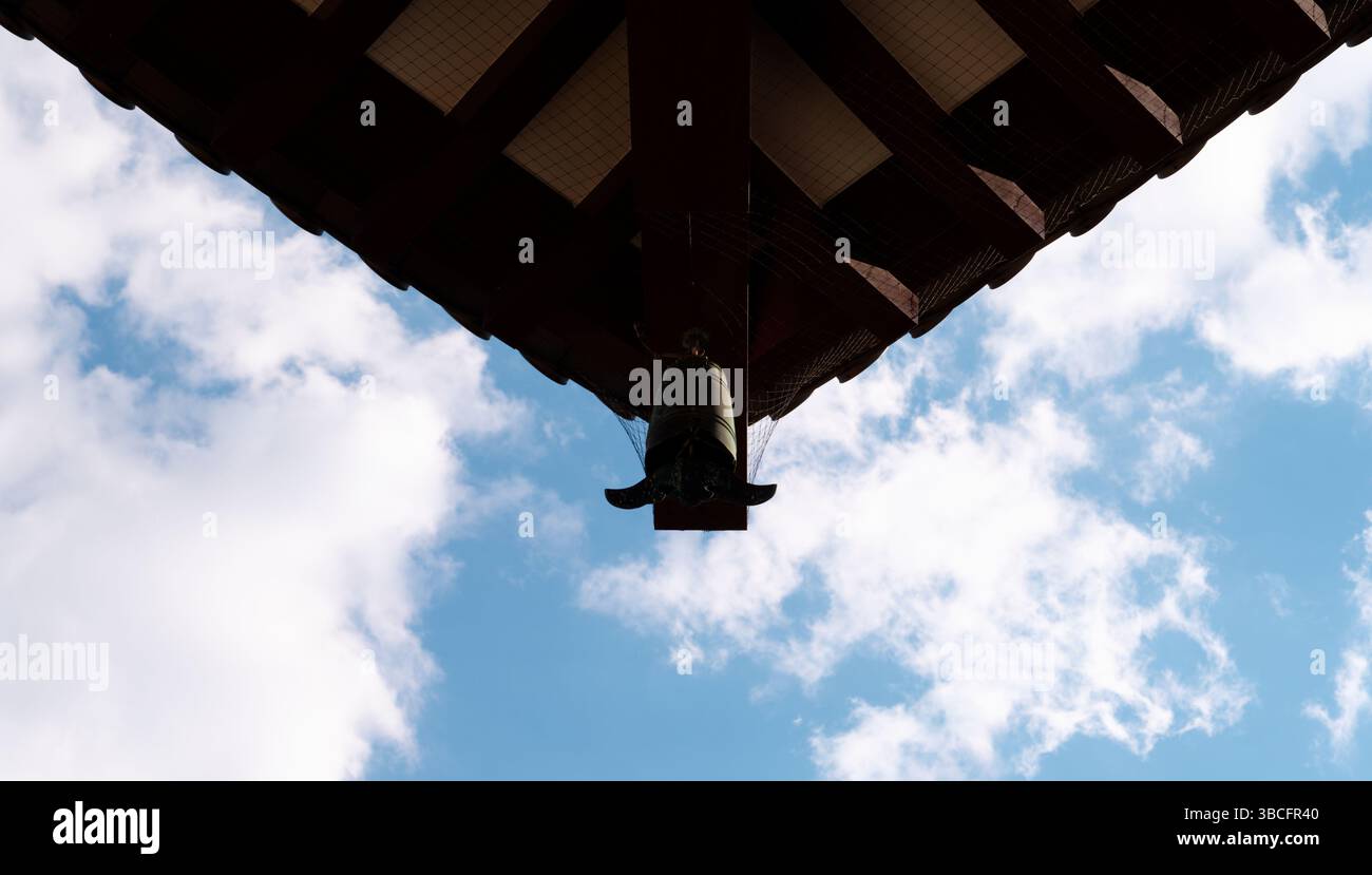 Eine Tempelglocke hängt unter den Traufen der Haupthalle von Zōjō-JI, die sich vor einem weichen Himmel befindet Stockfoto