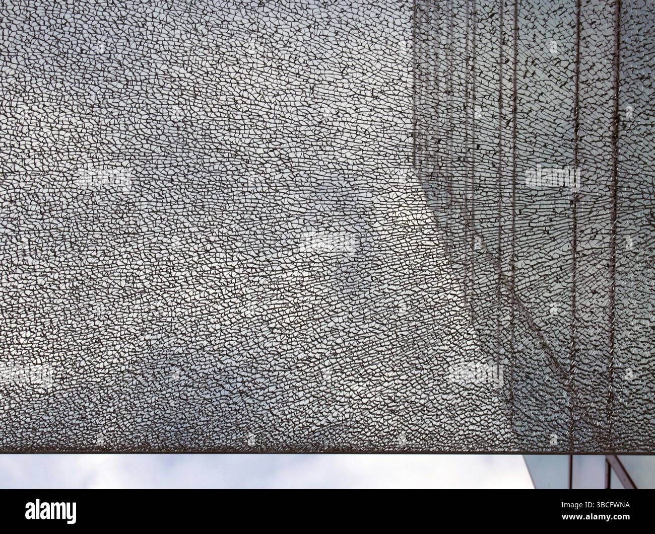 Eine Glasscheibe vor einem modernen Bürogebäude mit gerader Kante, die das Bild vor einem blau bewölkten Himmel teilt Stockfoto