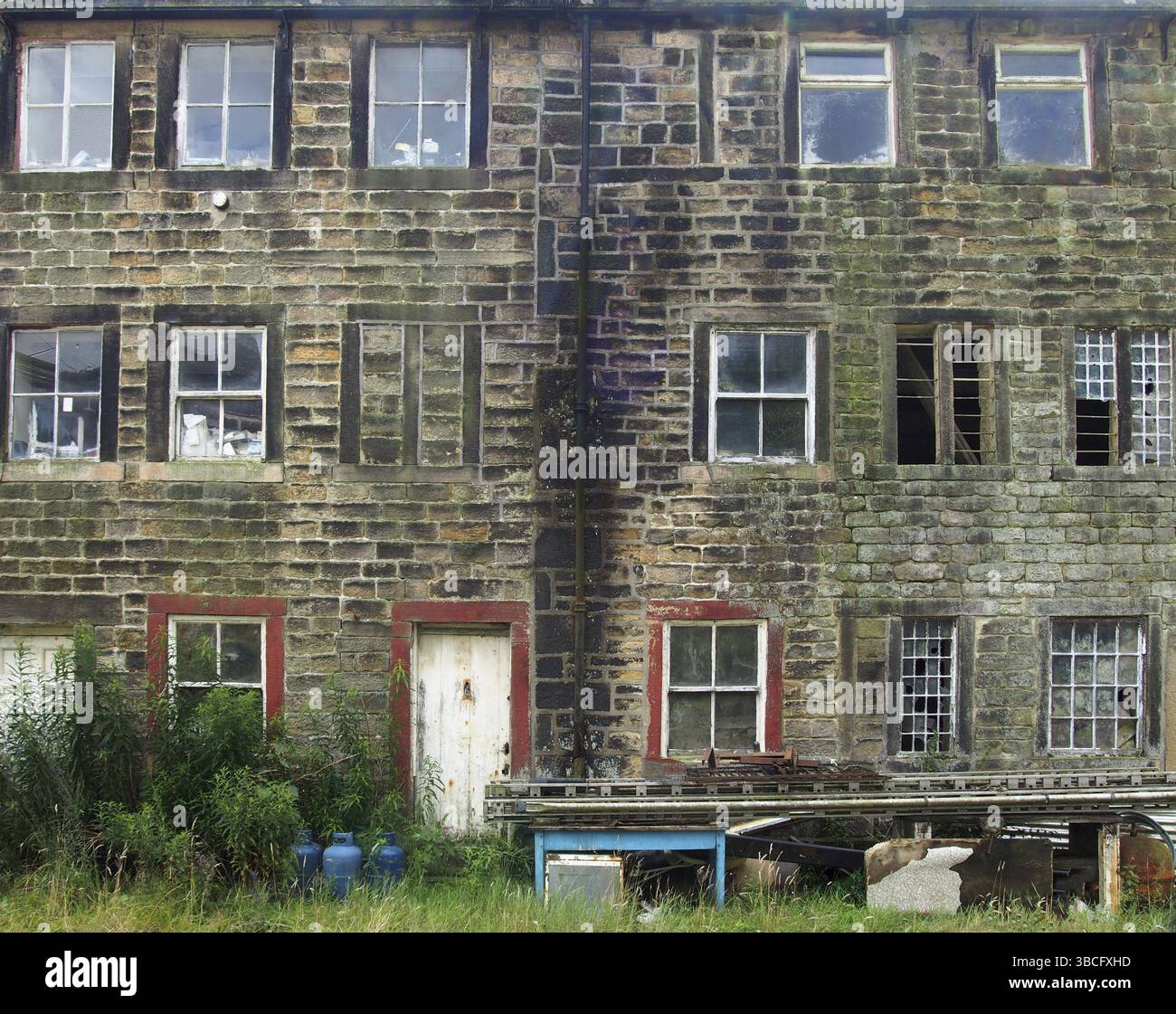 Die Fassade alter, verfallener Steinhäuser mit kaputten Fenstern und abblätternder roter Tür mit Schrott vor der Tür Stockfoto