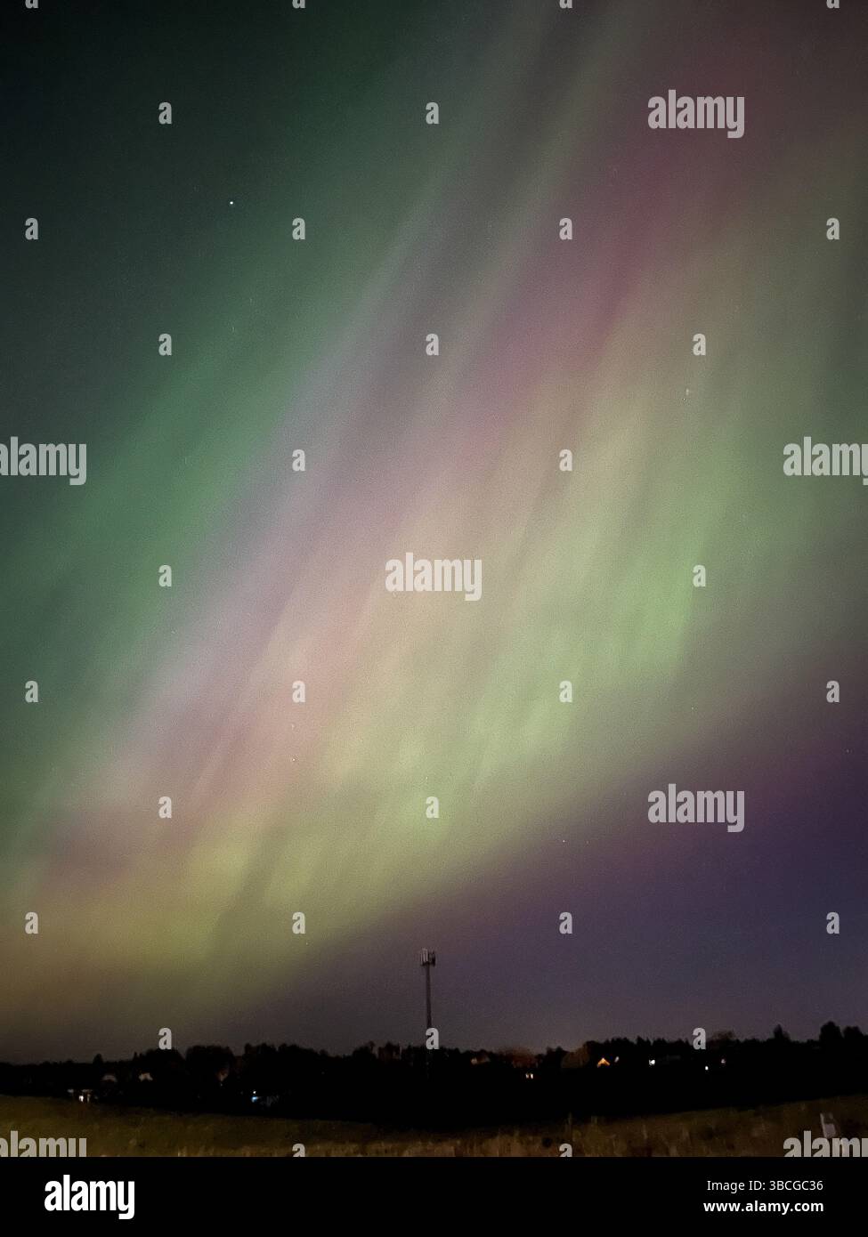 Nordlichter überziehen eine ruhige Stadt. Grüne und violette Farbtöne prägen den Nachthimmel in dieser magischen aurora. Stockfoto