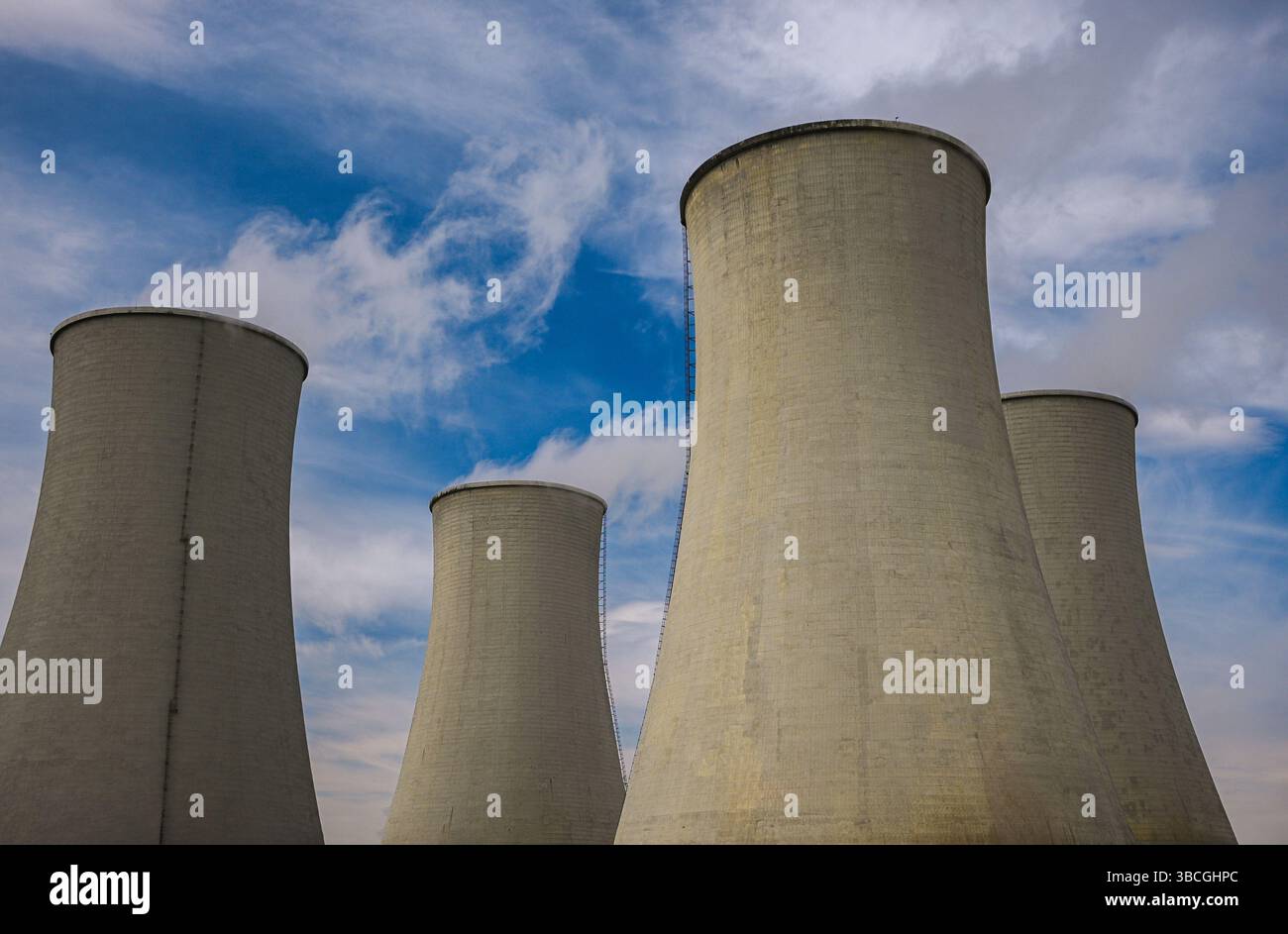 Große Kühltürme, die Dampf gegen einen bewölkten blauen Himmel in einer Stromerzeugungsanlage abgeben. Stockfoto