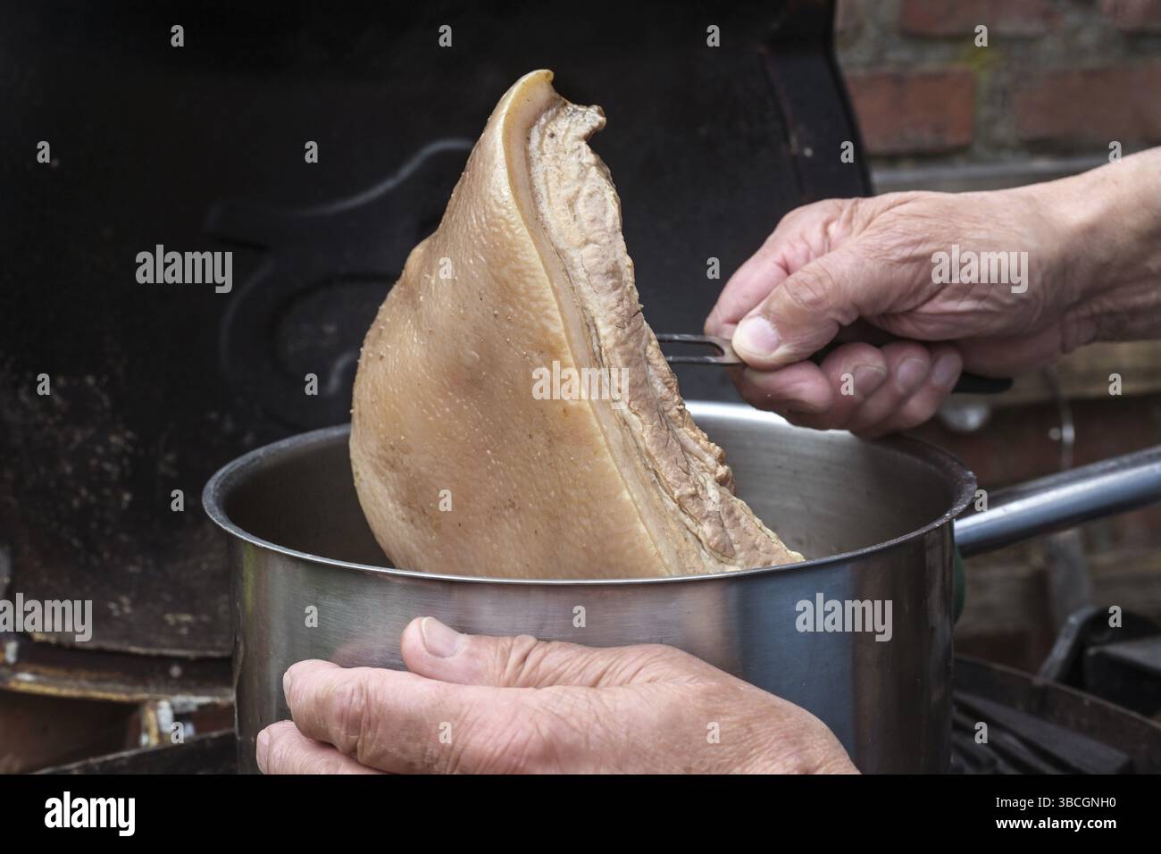 Der Koch nimmt ein Stück langsam gekochtes Rindenfleisch aus dem Topf, um eine Brühe in einer rustikalen Küche zu machen, Kopierraum, ausgewählter Fokus, enge Tiefe der fette Stockfoto