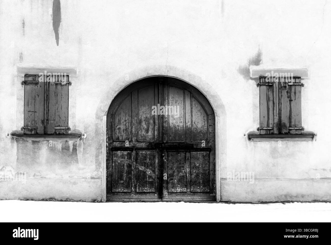 Monochromer Blick auf ein architektonisches Detail einer Hausfront mit Fenstern und einem großen Holztor und Schnee auf dem Boden im Dorf Maienfeld in Stockfoto